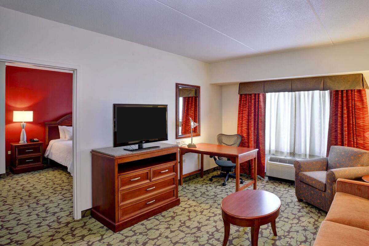 A hotel room with a bed, a desk with a TV, a chair, a small table, and a sofa.