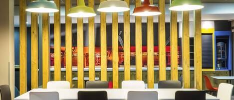 A modern dining area with a long table, black and white chairs, and colorful pendant lights.
