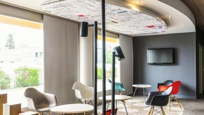 A modern interior with a curved ceiling, a large window, and a flat-screen TV mounted on the wall. - ibis Tarbes Odos (Odos)