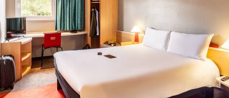 A hotel room with a large bed, a desk with a chair, a wardrobe, and a TV.