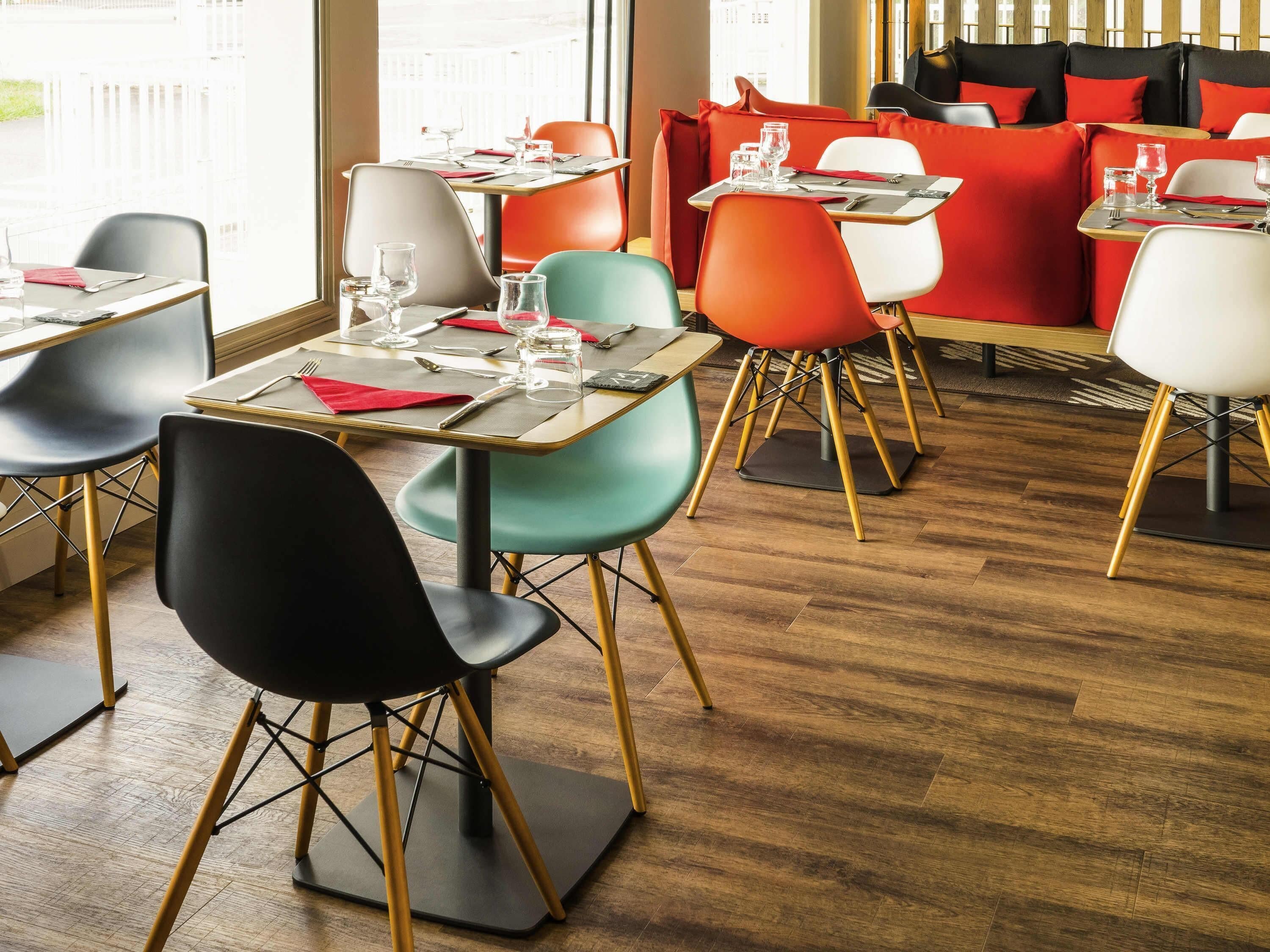 A modern restaurant interior with wooden flooring, multiple dining tables, and chairs with gold legs.