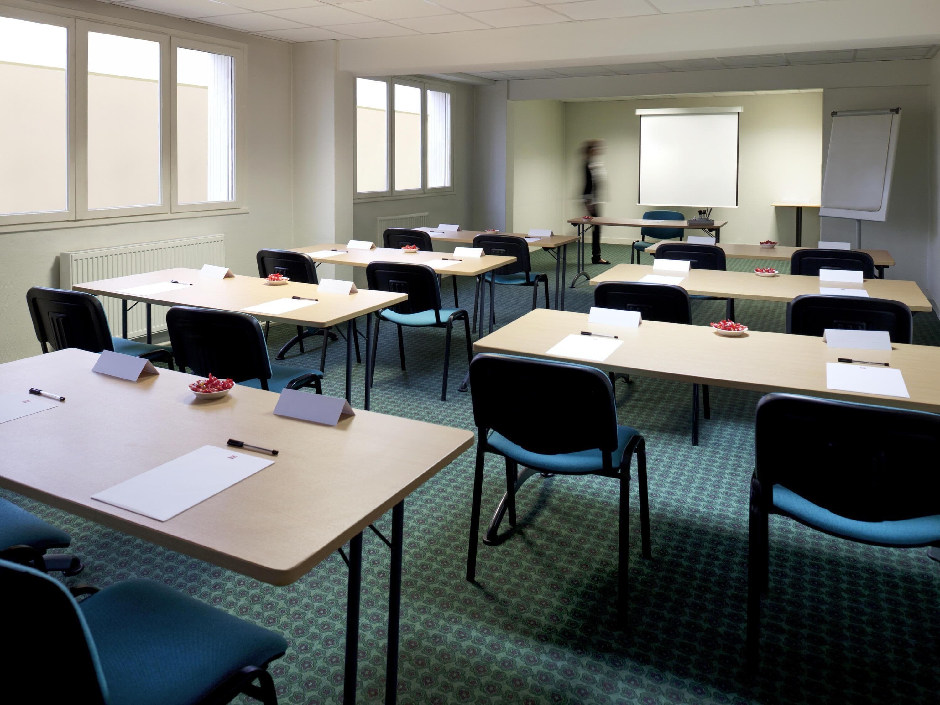 A conference room with multiple tables, chairs, a projector screen, and a whiteboard.