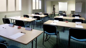 A conference room with multiple tables, chairs, a projector screen, and a whiteboard.