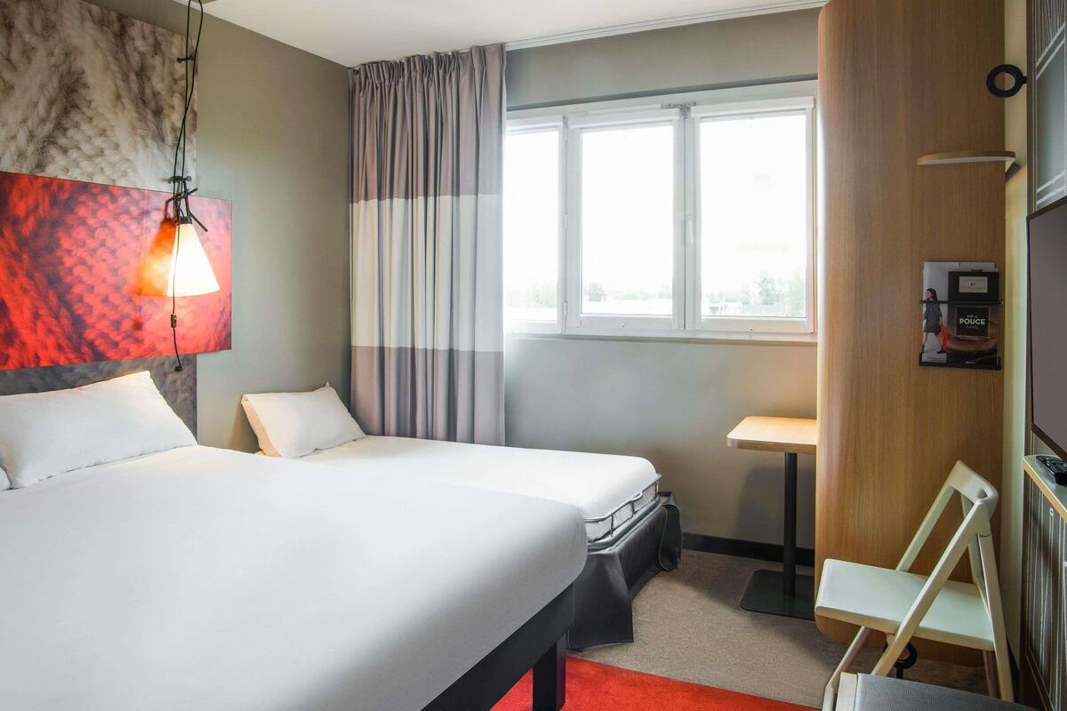 A hotel room with a large bed, a desk, a chair, a window with curtains, and a wall-mounted TV.