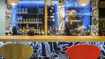 A bar area with shelves of bottles and glasses, a coffee machine, and a person working behind the counter.