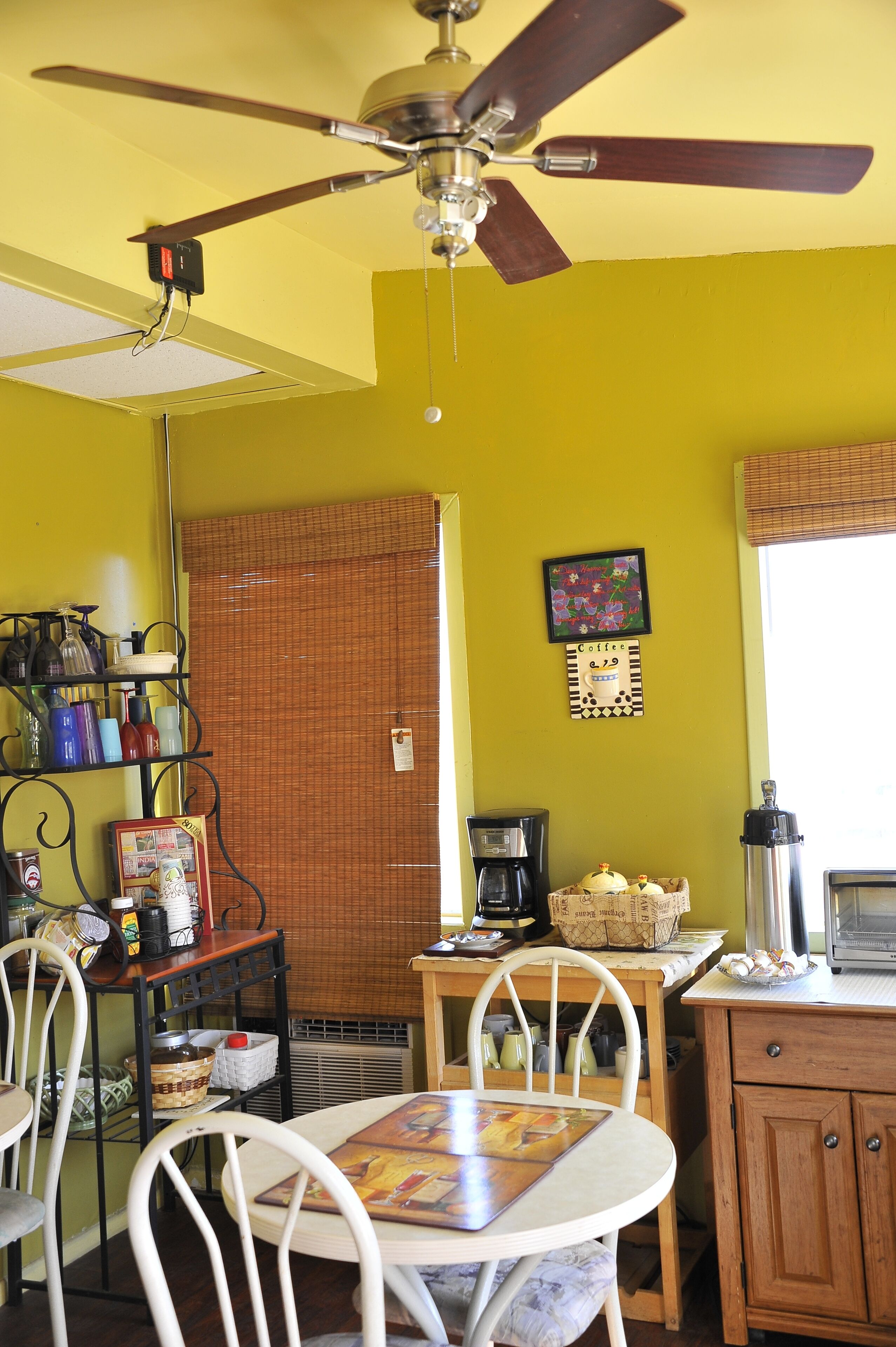 Une cuisine équipée d’un ventilateur de plafond, d’une machine à café, d’un réfrigérateur et d’une table à manger avec des chaises.