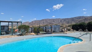 A swimming pool with lounge chairs and a covered area, surrounded by mountains. - Harmony Motel (Twentynine Palms)