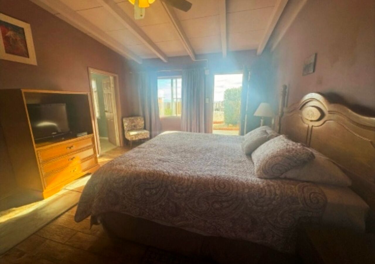 A bedroom with a bed, a dresser, a television, and a window with curtains.