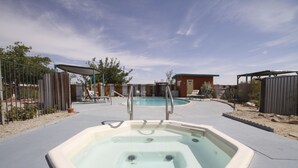 A hot tub in a backyard with a pool, lounge chairs, and a covered seating area. - Harmony Motel (Twentynine Palms)