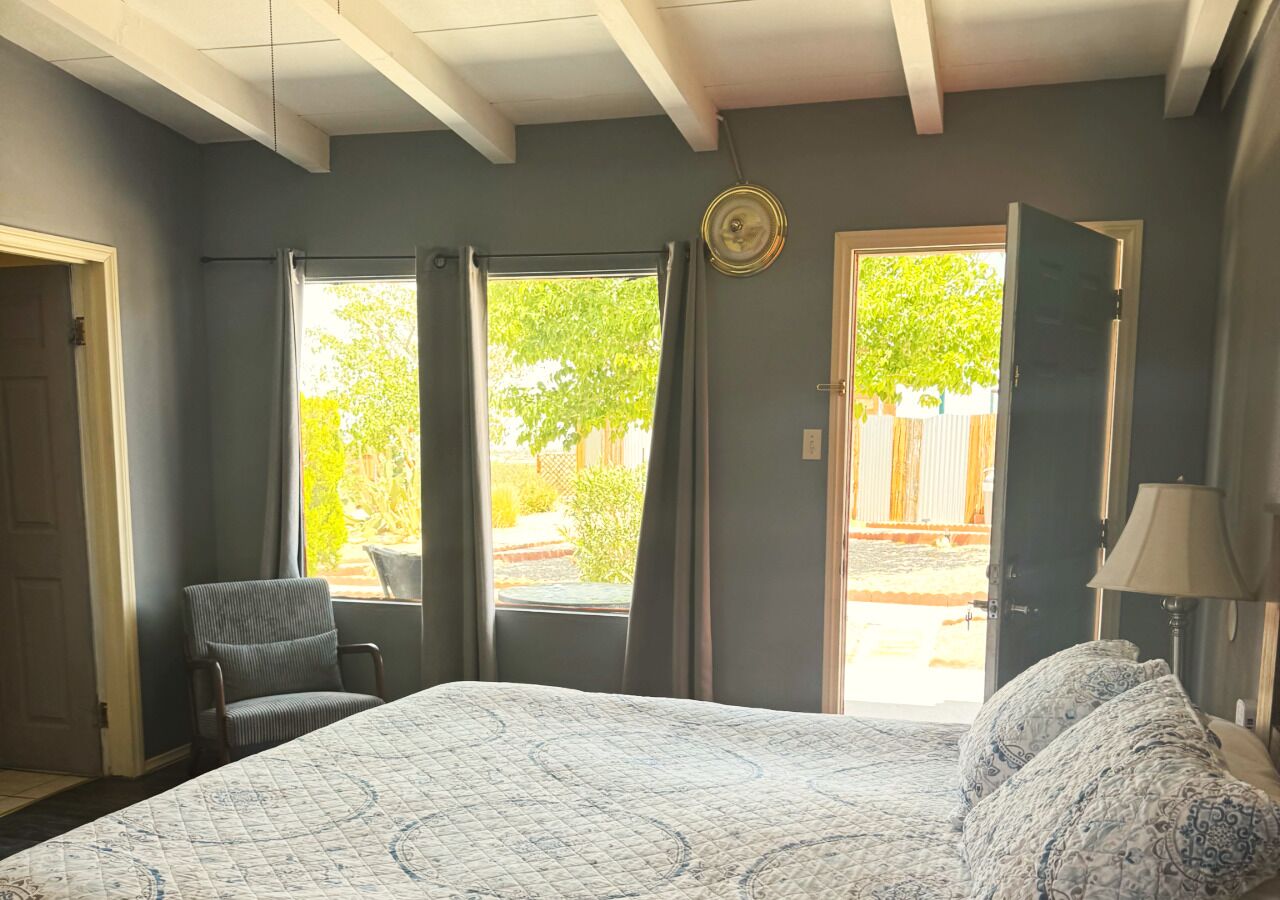 A bedroom with a large bed, a chair, a lamp, and a view of the outdoors through a door.