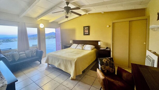 A bedroom with a bed, a desk, a chair, a ceiling fan, and a view of the sea. - Harmony Motel (Twentynine Palms)