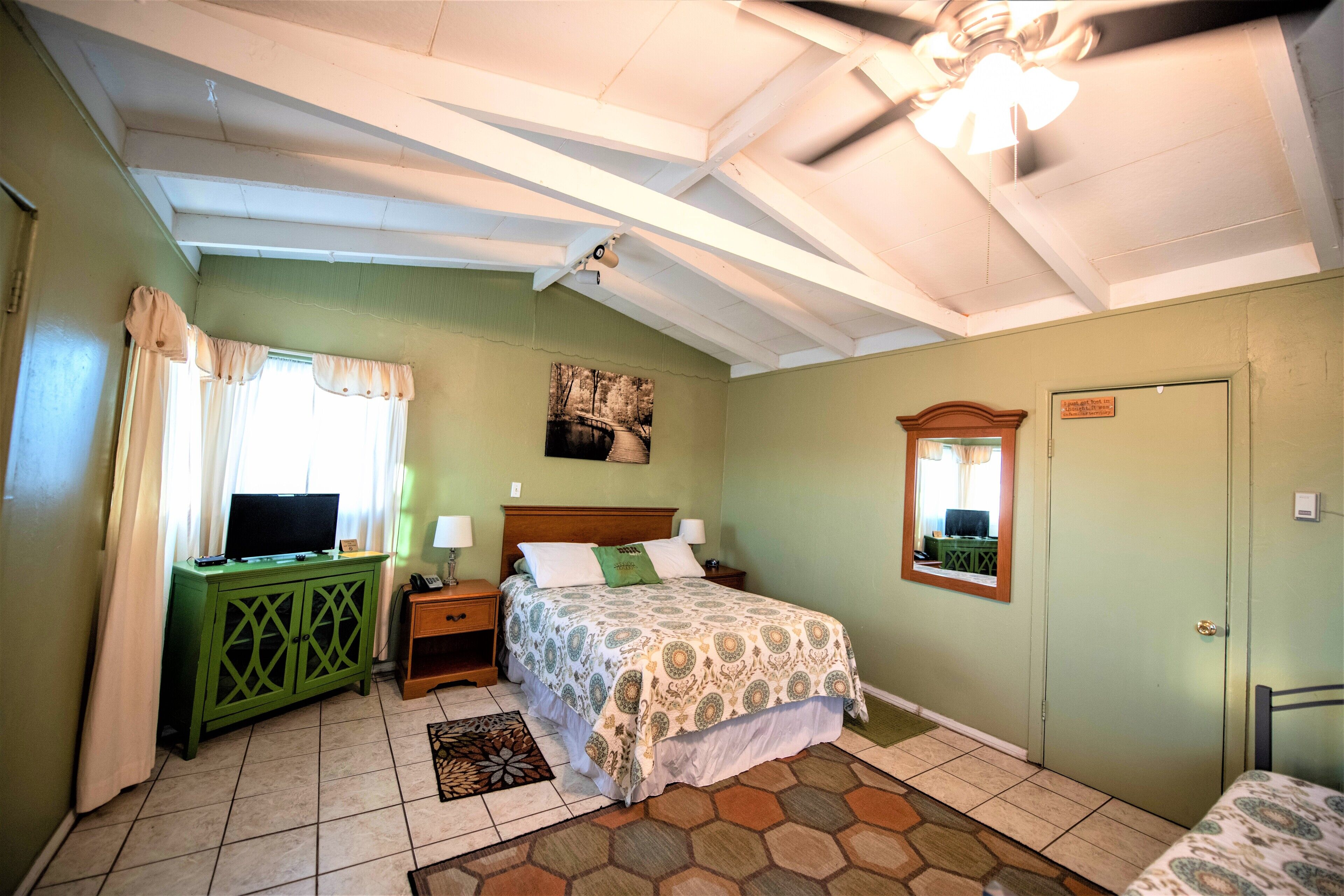 A bedroom with a bed, a green cabinet, a ceiling fan, and a window with curtains.