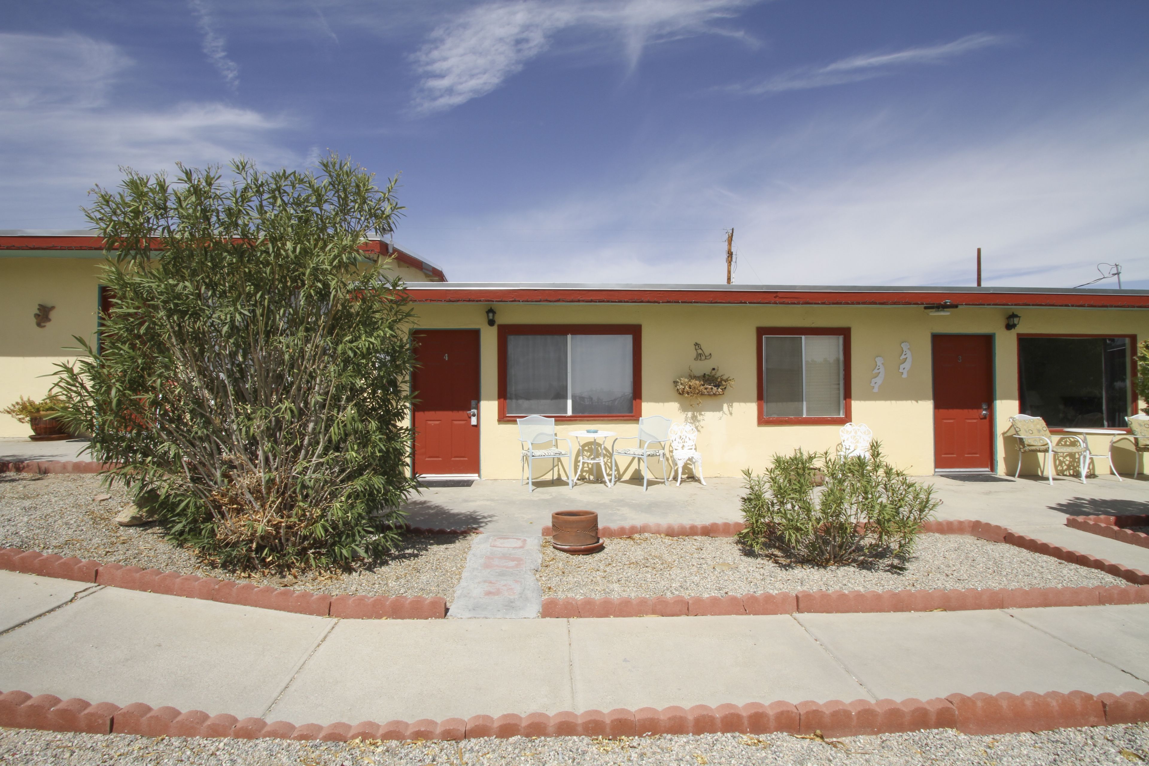 Un motel con una porta rossa, un piccolo giardino con un albero e un patio con sedie.