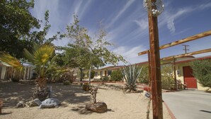 A desert landscape with cacti and a wooden structure. - Harmony Motel (Twentynine Palms)