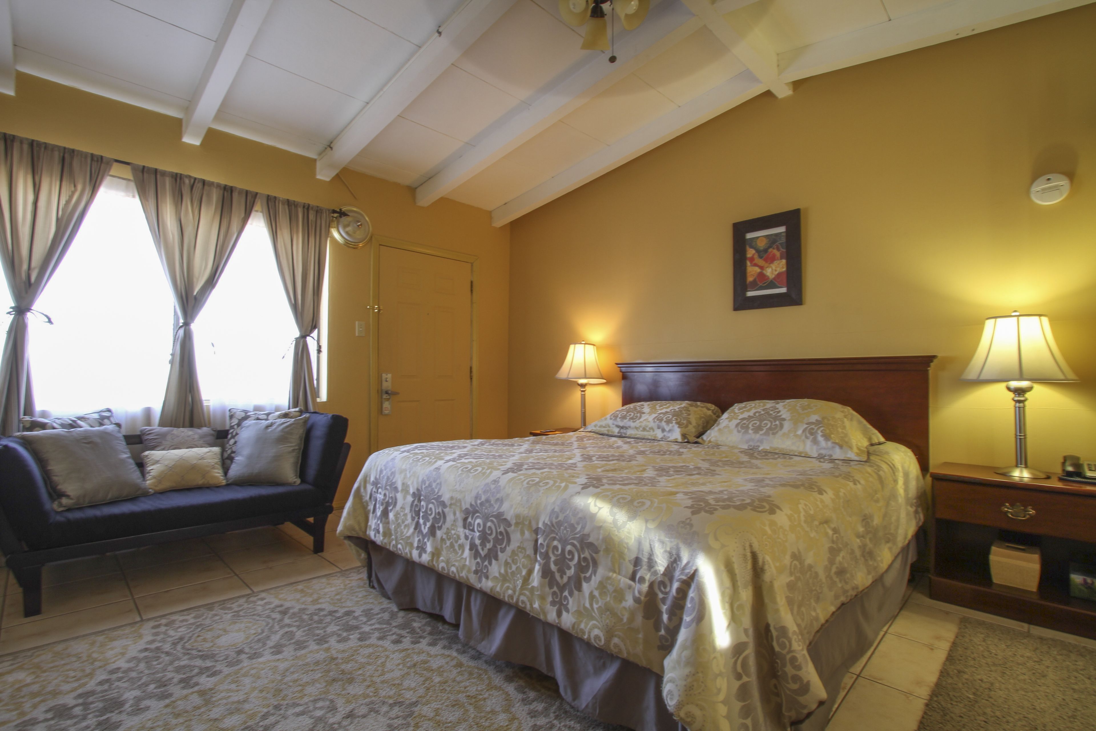 A bedroom with a bed, a sofa, a nightstand, and a lamp.