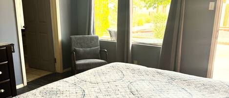 A bedroom with a bed, a chair, a window, and a door.