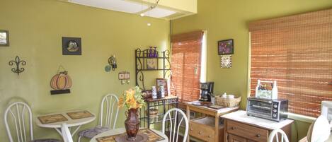 A dining area with a round table, white chairs, a ceiling fan, and a window with blinds.
