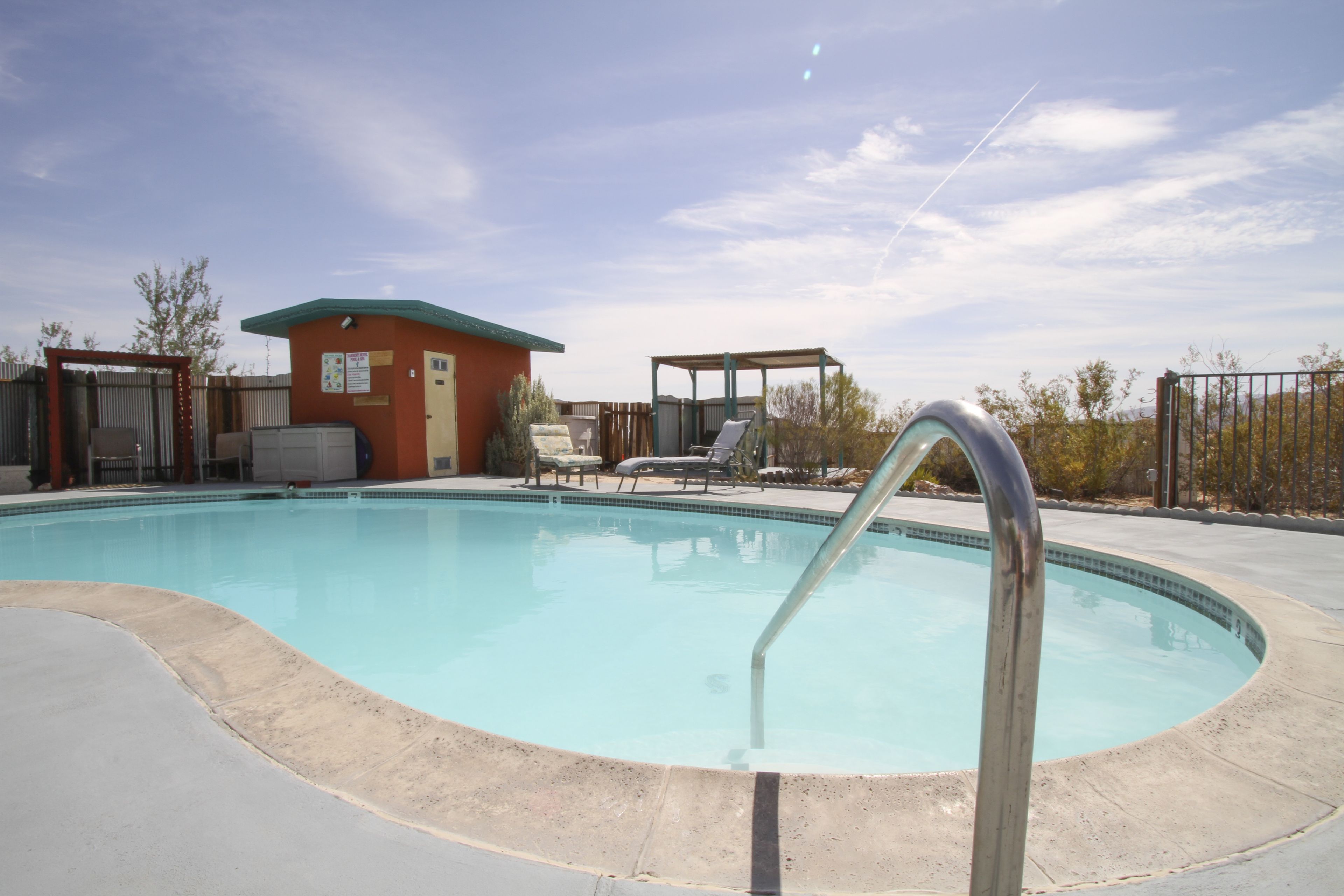 A swimming pool with a metal ladder, lounge chairs, and a small building with a green roof.