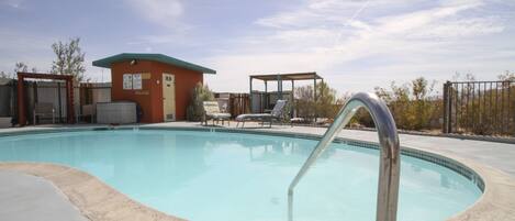 A swimming pool with a metal ladder, lounge chairs, and a small building with a green roof.