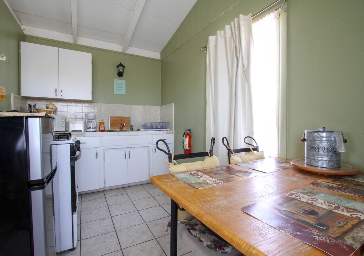 A kitchen with white cabinets, a refrigerator, a coffee maker, and a table with a placemat.