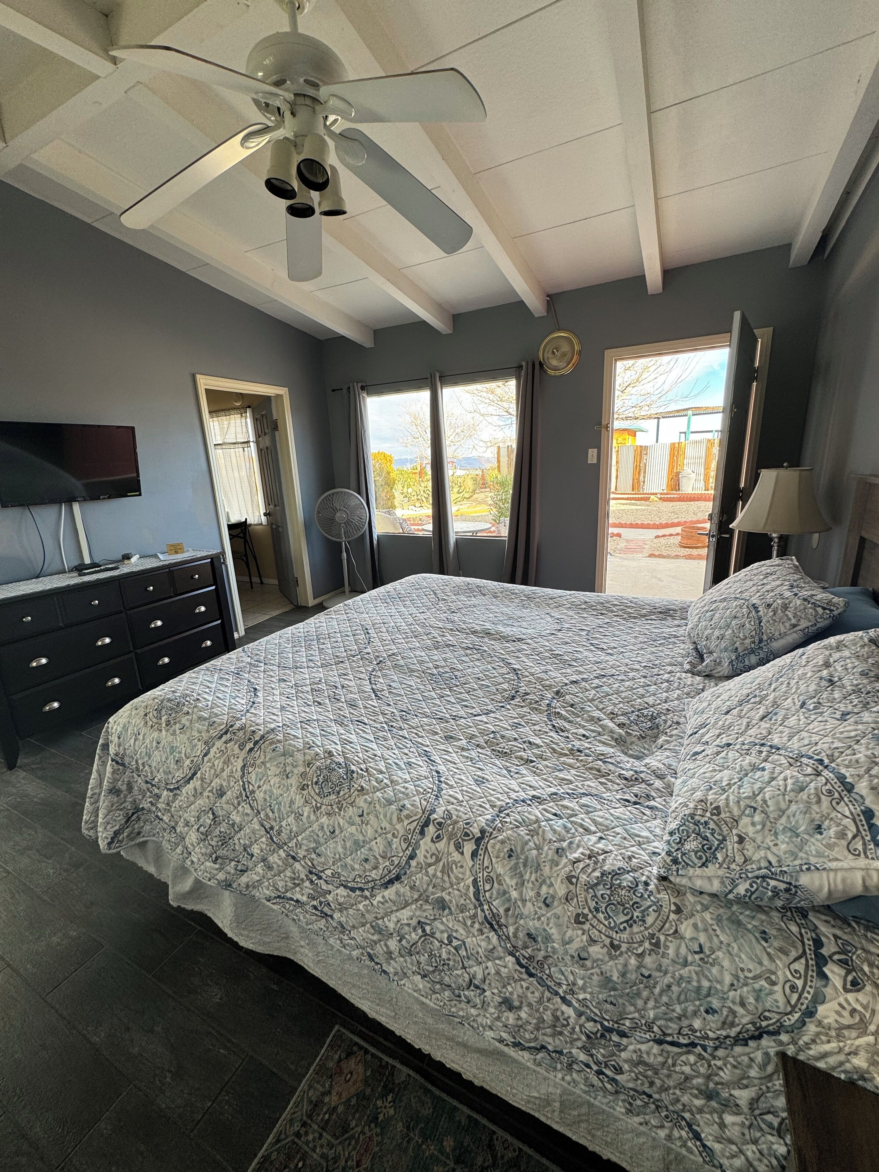Un dormitorio con una cama grande, un ventilador de techo, un televisor y vistas al exterior a través de una ventana.