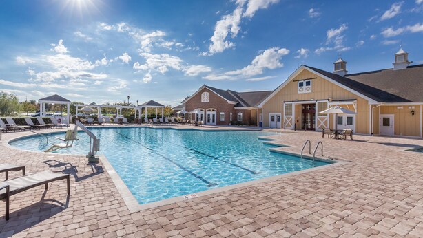A swimming pool with lounge chairs and a covered area, surrounded by buildings with a brick facade and a clear blue sky. - Club Wyndham Governor’s Green (Williamsburg)