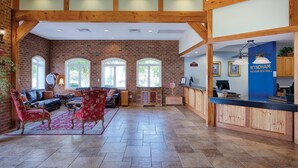 A spacious lobby with a brick wall, wooden beams, a reception desk, and a seating area with red upholstered chairs. - Club Wyndham Governor’s Green (Williamsburg)