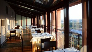 A restaurant with tables set for dining, large windows, and a view of the city. - Hotel Cigarral El Bosque (Toledo)