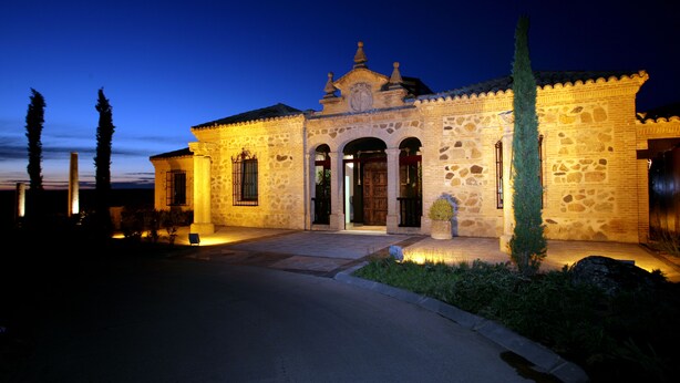 A stone building with a central entrance, arched doorways, and a decorative roof. - Hotel Cigarral El Bosque (Toledo)