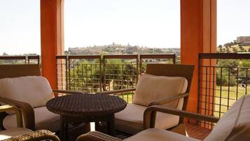 A balcony with wicker furniture, including two chairs and a small table, overlooking a cityscape.