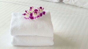 A neatly folded white towel with a purple and white orchid on top, placed on a bed with white bedding. - California Suites Motel (Calexico)