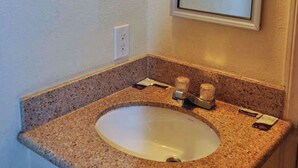 A bathroom with a granite countertop sink, a mirror above it, and a white wall. - California Suites Motel (Calexico)