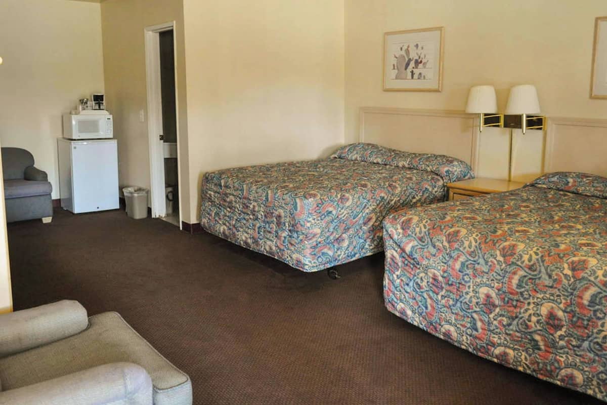 A hotel room with two beds, a small desk, a chair, a microwave, and a door leading to a bathroom.