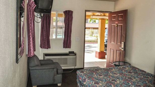 A small room with a bed, a chair, a heater, and a TV mounted on the wall. - California Suites Motel (Calexico)