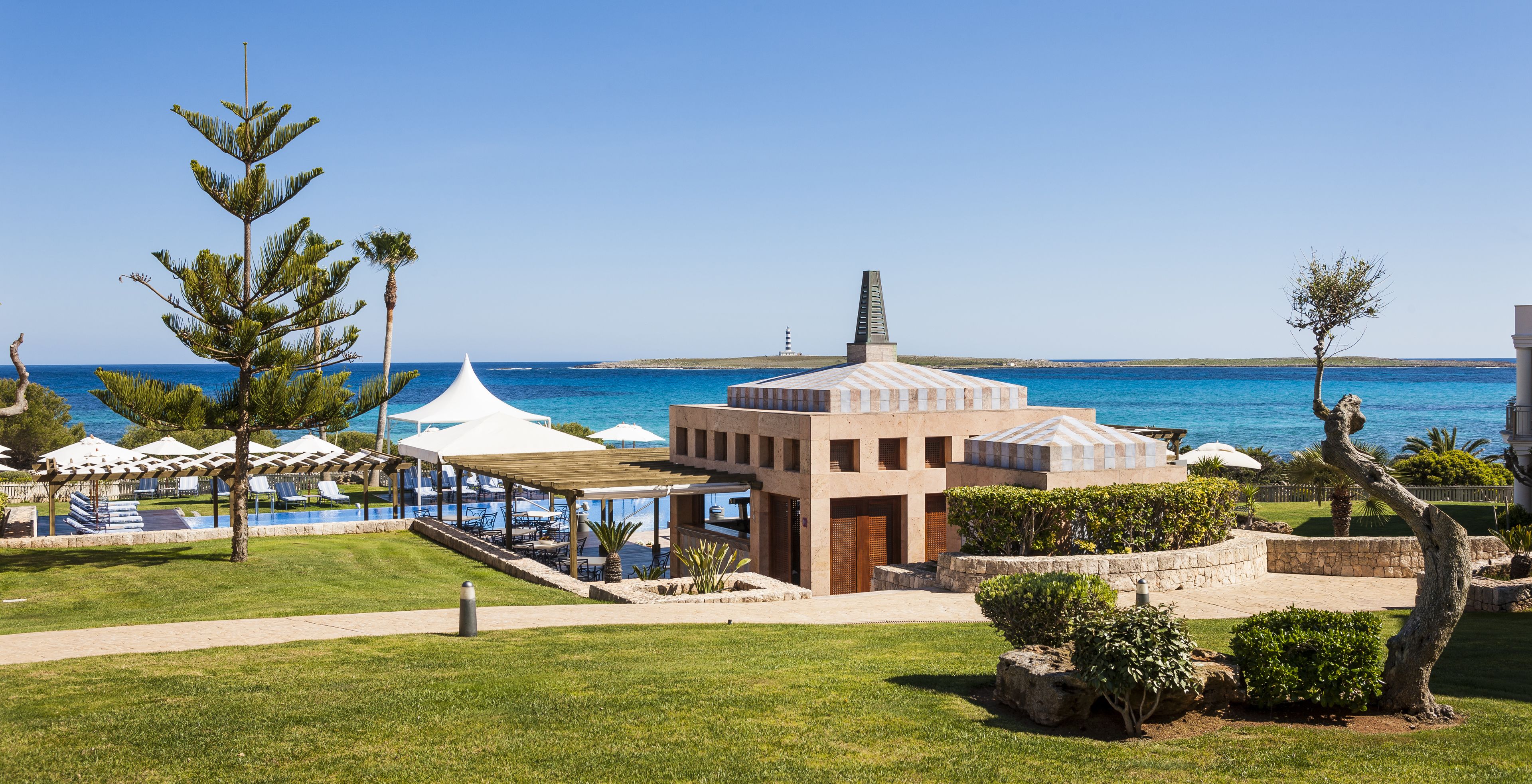 Un resort con zona de piscina, mobiliario exterior y vistas al mar.