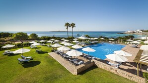 A pool area with lounge chairs and umbrellas, surrounded by greenery and a view of the sea. - Insotel Punta Prima Prestige Suites & Spa (Sant Lluis)