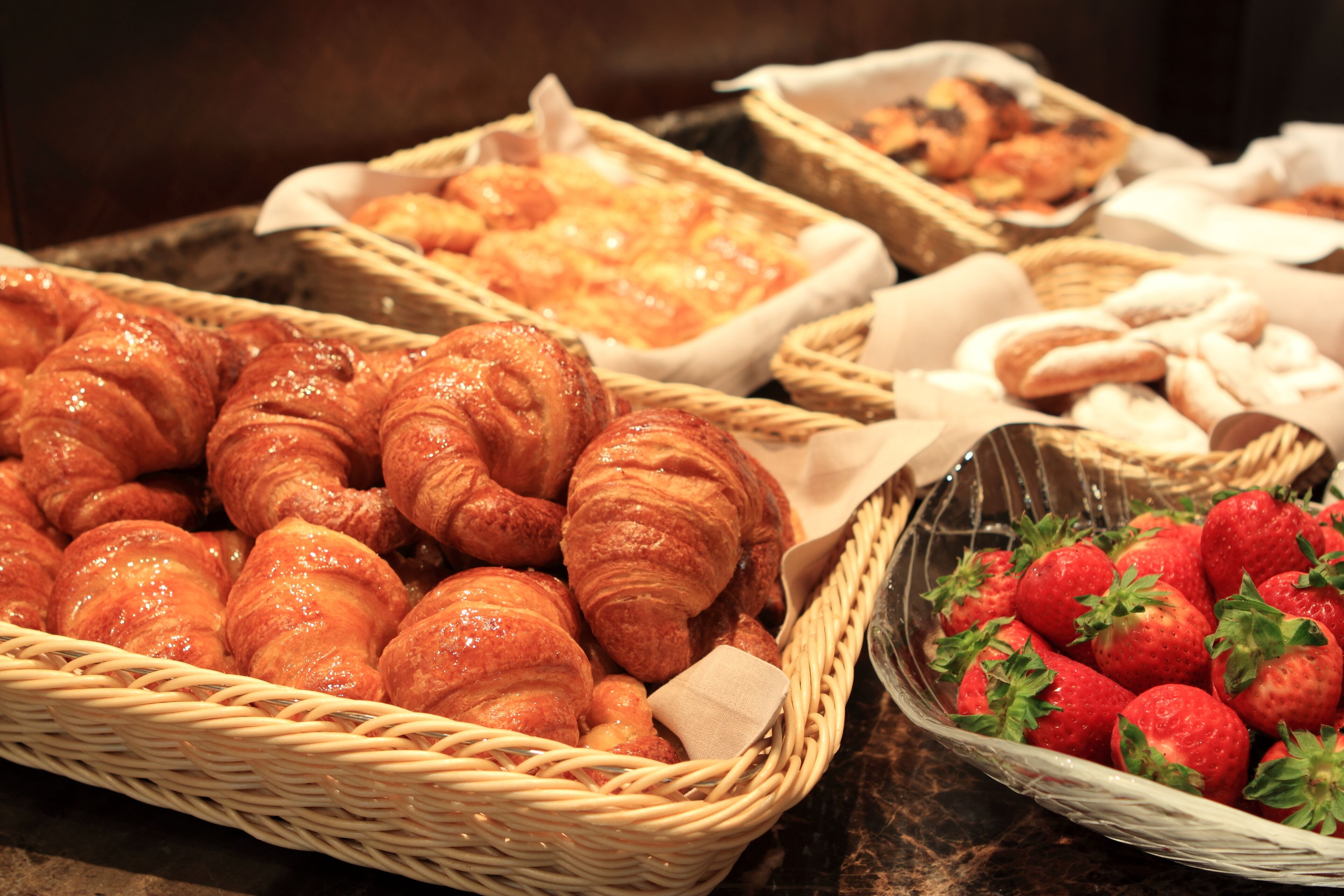 Verschillende gebakjes, waaronder croissants en aardbeien, in manden.