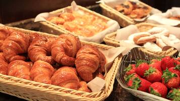 Verschillende gebakjes, waaronder croissants en aardbeien, in manden.