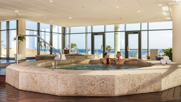 A hot tub area with a view of the sea, a palm tree, and a chair. - Insotel Punta Prima Prestige Suites & Spa (Sant Lluis)
