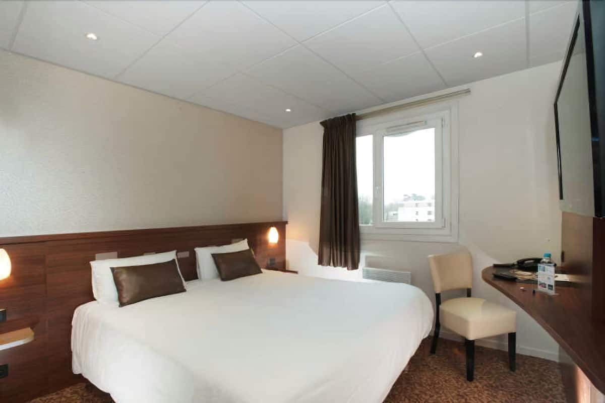 A hotel room with a large bed, a desk, a chair, and a television.