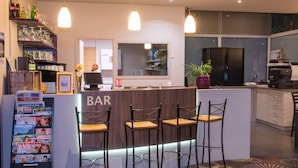 A modern bar area with three stools, a refrigerator with magazines, and a potted plant.