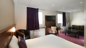 A hotel room with a large bed, a desk, a chair, a sofa, and a TV mounted on the wall.