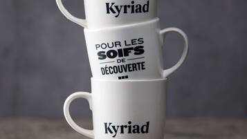 Tres tazas blancas de café apiladas con texto, sobre una superficie con granos de café esparcidos.