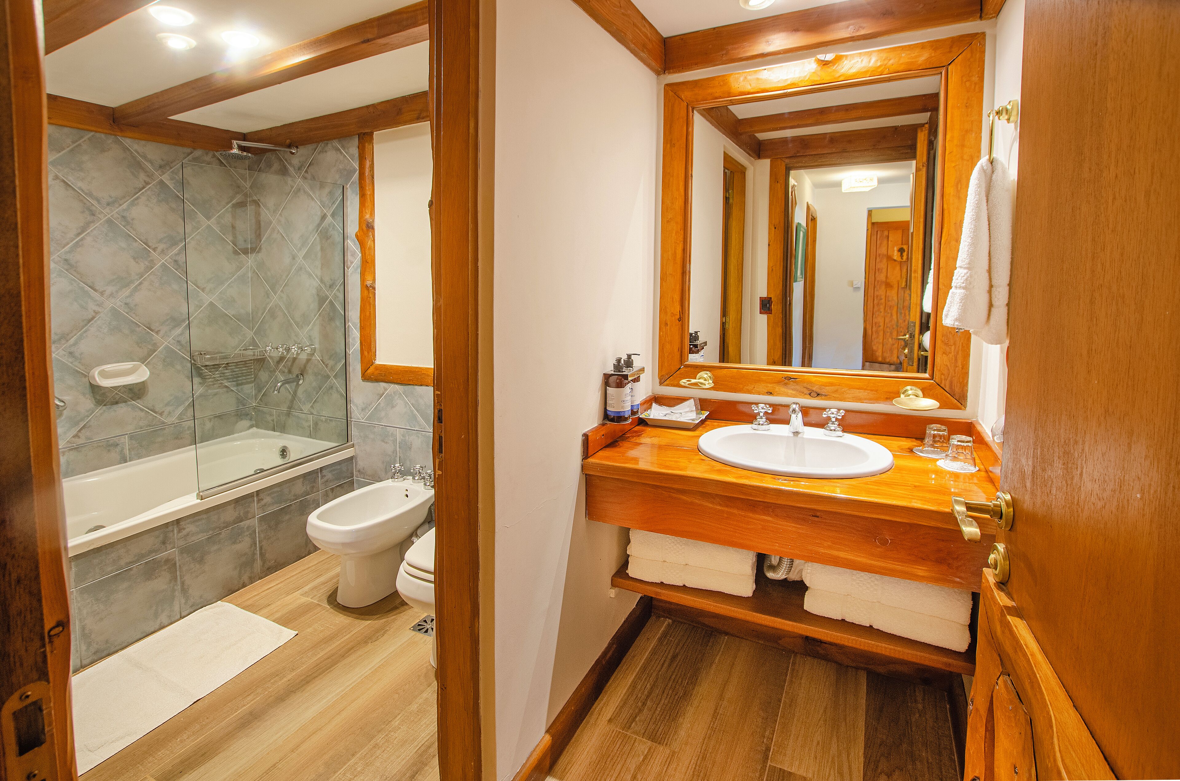 A bathroom with a wooden vanity, a large mirror, a bathtub, and a toilet.