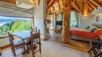 A wooden interior with a dining area, a bed, and a view of a lake.
