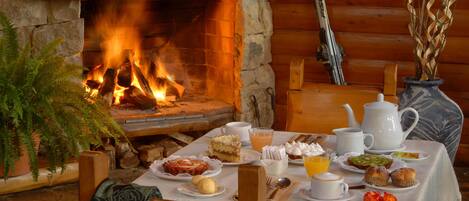 A cozy breakfast setup with a stone fireplace, wooden furniture, and a variety of breakfast items.