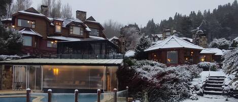 Un espacio exterior cubierto de nieve con piscina, edificios de madera y una escalera que sube.