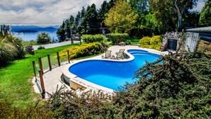 Una piscina con sillas de descanso, rodeada de exuberante vegetación y vistas a un lago y montañas.