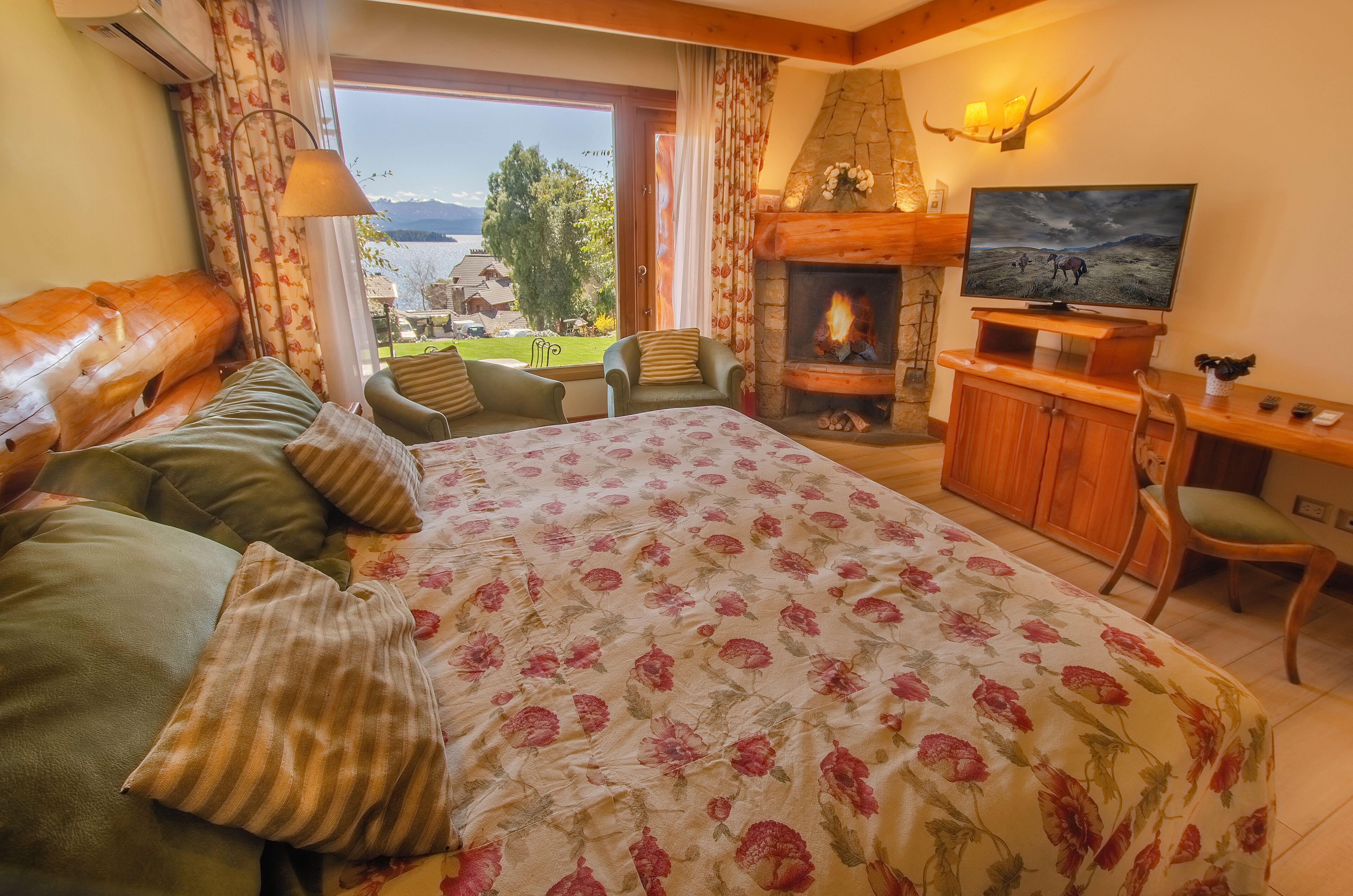 A cozy bedroom with a large bed, a fireplace, a TV, and a view of the outdoors.
