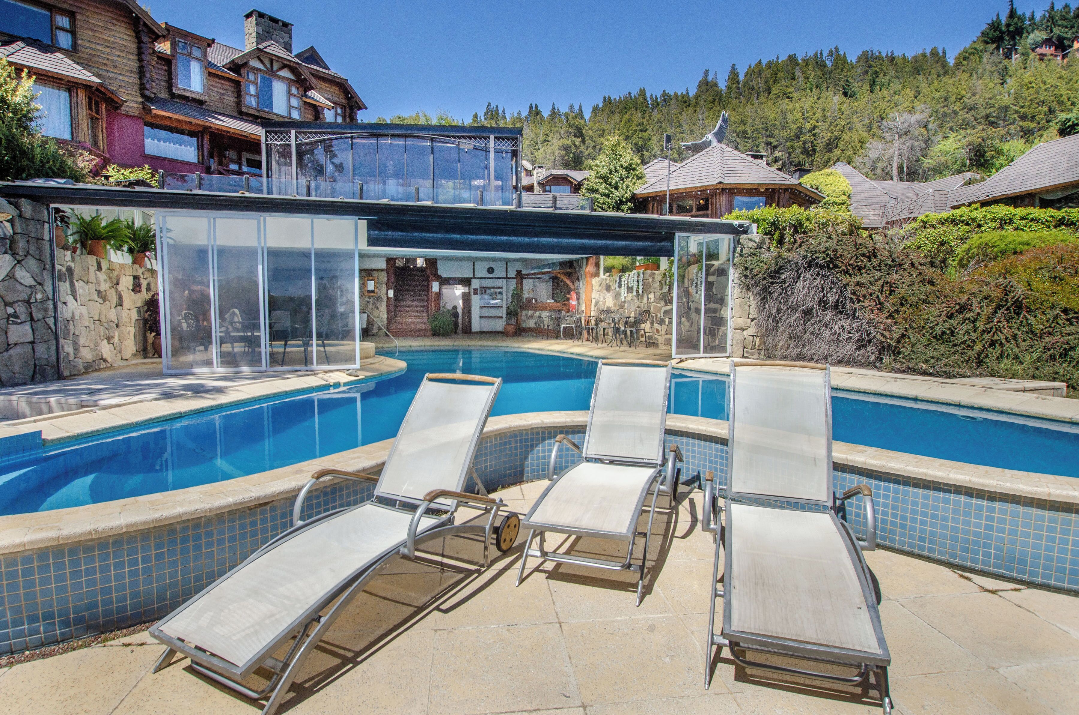 Un espace piscine avec des chaises longues, un coin salon abrité et un mur en pierre.
